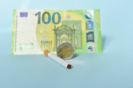 Cigarettes and money on blue background. Euro banknotes and coins, cost of smoking, cigarette price concept. Selective focusの写真素材
