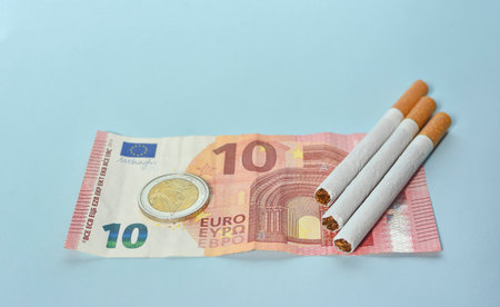 Cigarettes and money on blue background. Euro banknotes and coins, cost of smoking, cigarette price concept. Selective focusの写真素材