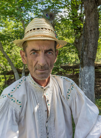 Salaj, Transylvania, Romania-May 14, 2018: portrait of a Romanian peasant with blue eyes wearing a traditional folk shirt and a hat in summer dayのeditorial素材