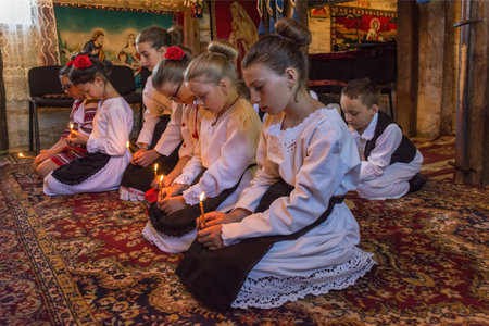 Salaj, Romania-May 13, 2018: Children wearing traditional Romanian costumes praying with faith in a old wooden church in Transylvania region, Romania. Low light, selective focusのeditorial素材