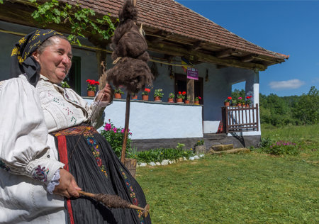Salaj, Transylvania, Romania-May 14, 2018: old woman dressed in traditional Romanian folk costume, spinning wool in front of her charming houseのeditorial素材