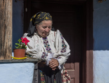 Salaj, Transylvania, Romania-May 14, 2018: old woman dressed in traditional Romanian folk costume sitting on the terrace of her little charming houseのeditorial素材