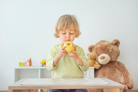 Cute happy child boy having fun eating a big fresh yellow apple fruit at home. Children healthy eating and lifestyle conceptual photoの写真素材