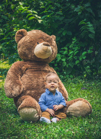 Sweet little baby boy having fun outdoors playing with his giant teddy bear in the parkの写真素材