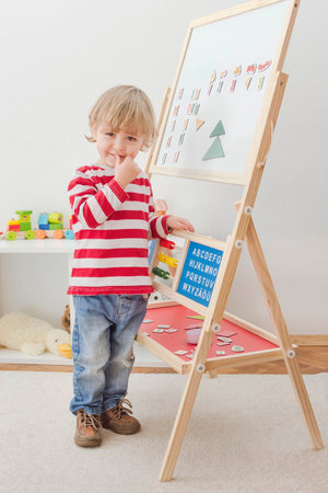 Cute little child playing at a magnetic board, learning letters, numbers and geometric shapes at home. Educative and funny indoor activity for early development.の写真素材