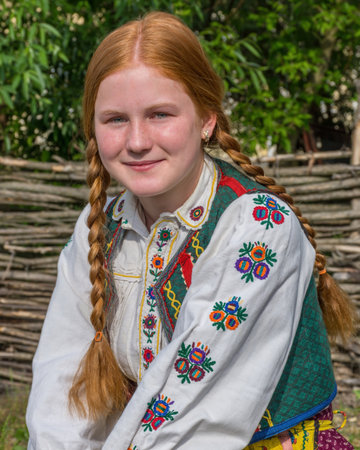 Salaj, Transylvania, Romania-May 14, 2018: beautiful freckled young girl with red hair and blue eyes in traditional Romanian folk costume in Marin village, Salaj county, Romaniaのeditorial素材