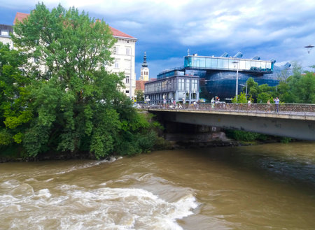 Graz,Austria-17.08.2020:Mur river, Love Bridge and Kunsthaus Graz, the modern Art Museum for contemporary art, looking like a alien in the middle of Graz's old architectureのeditorial素材
