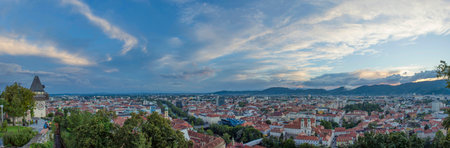 Cityscape of Graz and the clock tower (Grazer Uhrturm), famous tourist attraction on Shlossberg hill, Graz, Styria region, Austria, at sunset. Dramatic sky, panoramic viewのeditorial素材