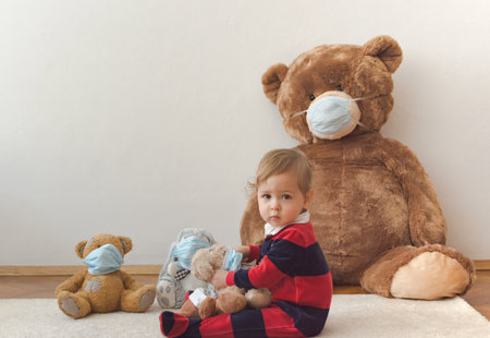 Child playing with his sick teddy bears wearing medical mask against viruses. Role playing, child playing doctor with plush toy. Children and illness concept.の写真素材