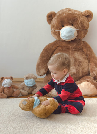 Child playing with his sick teddy bears wearing medical mask against viruses. Role playing, child playing doctor with plush toy. Children and illness concept.の写真素材