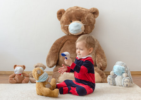 Child playing with his sick teddy bears wearing medical mask against viruses. Role playing, child playing doctor with plush toy. Children and illness concept.の写真素材