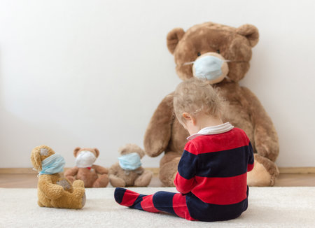 Child playing with his sick teddy bears wearing medical mask against viruses. Role playing, child playing doctor with plush toy. Children and illness concept.の写真素材