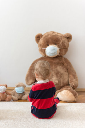 Child playing with his sick teddy bears wearing medical mask against viruses. Role playing, child playing doctor with plush toy. Children and illness concept.の写真素材