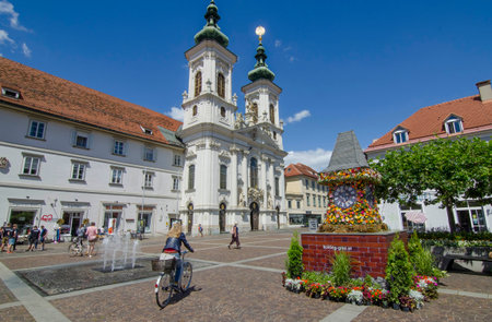 Graz,Austria-July 07, 2020: The famous clock tower, one of the city main attractions, made of flowers and Mariahilfer church and square in sunny day, Styria region, Austriaのeditorial素材
