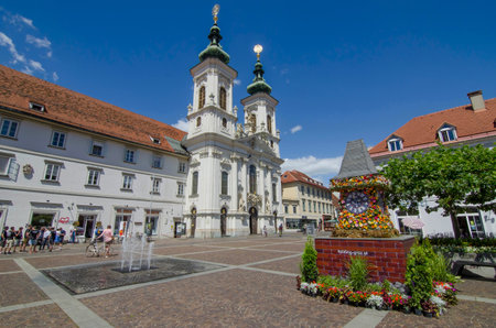 Graz,Austria-July 07, 2020: The famous clock tower, one of the city main attractions, made of flowers and Mariahilfer church and square in sunny day, Styria region, Austriaのeditorial素材
