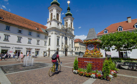 Graz,Austria-July 07, 2020: The famous clock tower, one of the city main attractions, made of flowers and Mariahilfer church and square in sunny day, Styria region, Austriaのeditorial素材
