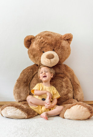 Sweet happy child boy playing with his giant teddy bear, indoor at homeの写真素材