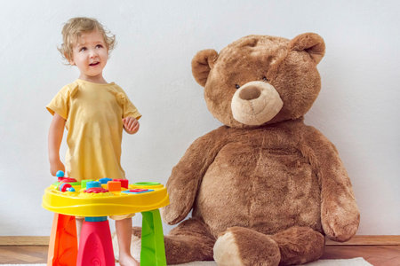 Sweet happy child boy having fun playing at a colorful table of activities with his giant teddy bear, indoor at homeの写真素材