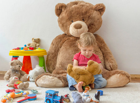 Sweet happy child boy having fun playing with his giant teddy bear and many colorful toys, indoor at homeの写真素材