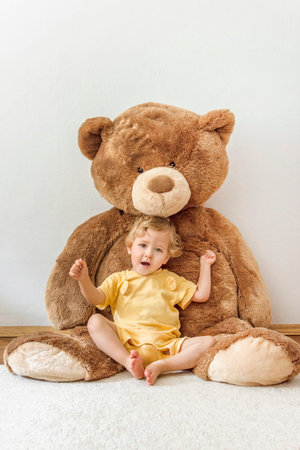 Sweet happy child boy playing with his giant teddy bear, indoor at homeの写真素材