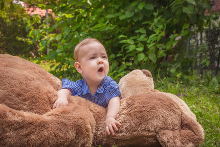 Sweet little baby boy having fun outdoors playing with his giant teddy bear in the parkの写真素材