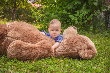 Sweet little baby boy having fun outdoors playing with his giant teddy bear in the parkの写真素材