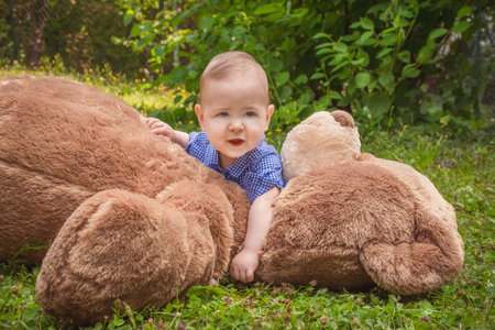 Sweet little baby boy having fun outdoors playing with his giant teddy bear in the parkの写真素材