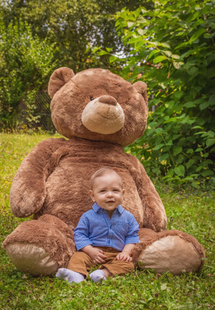Sweet little baby boy having fun outdoors playing with his giant teddy bear in the parkの写真素材
