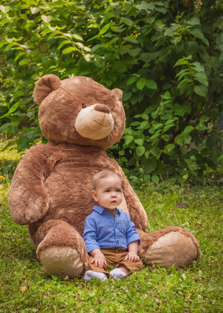 Sweet little baby boy having fun outdoors playing with his giant teddy bear in the parkの写真素材