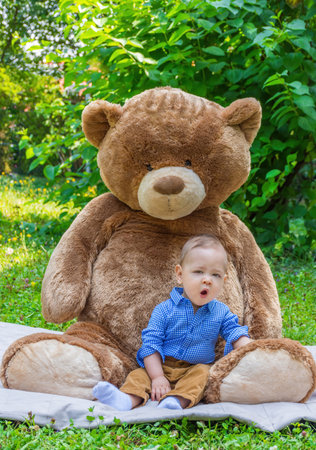 Sweet little baby boy having fun outdoors playing with his giant teddy bear in the parkの写真素材