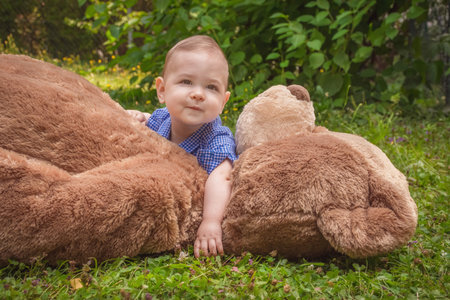 Sweet little baby boy having fun outdoors playing with his giant teddy bear in the parkの写真素材