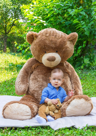 Sweet little baby boy having fun outdoors playing with his giant teddy bear in the parkの写真素材