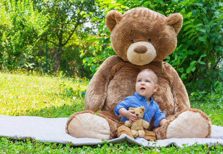 Sweet little baby boy having fun outdoors playing with his giant teddy bear in the parkの写真素材