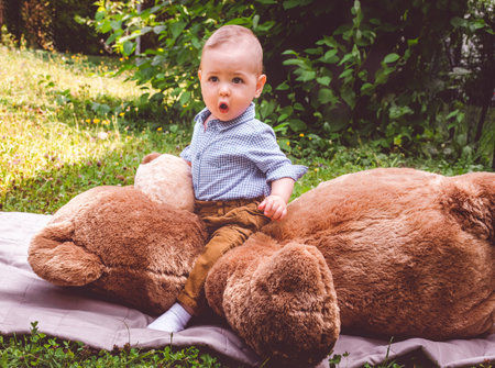 Sweet little baby boy having fun outdoors playing with his giant teddy bear in the parkの写真素材