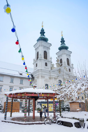Graz, Austria - December 09, 2021: People walking through the snow in front of the beautiful Mariahilfer church, in Graz, Steiermark, Austria, in winter dayのeditorial素材