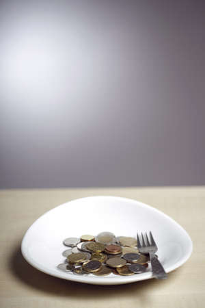Many coins on a white plate and a forkの写真素材