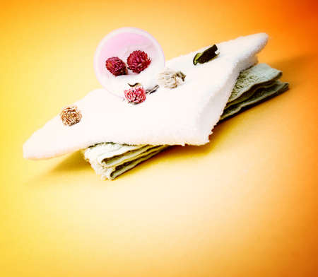 Spa essentials (cream, white towel and pink flowers) isolated on yellowの写真素材