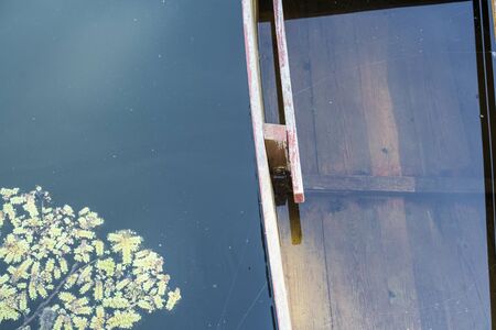 Fragment of partly drowned fishing boat with red oar still attached in some green water of the river with floating watermossの写真素材