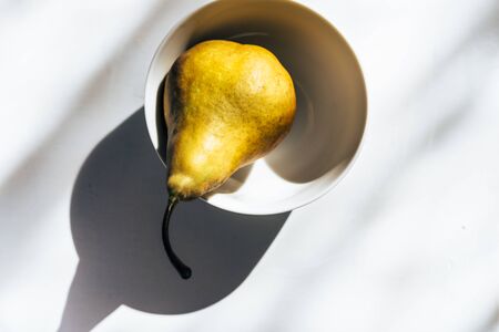 Ripe yellow pear in white porcelain bowl on white backgroundの写真素材