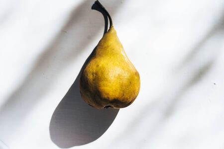 Ripe yellow pear casting shadow on white tableの写真素材