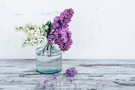 Branches of lilac in transparent glass vase on vintage wooden table with white backgroundの写真素材