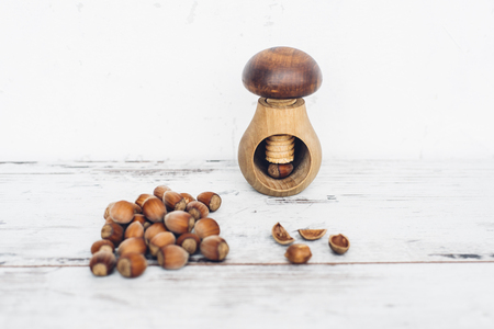Hazelnuts in pile on wooden table with one mushroom-shaped nut in the nut-cracker and one nut cracked openの写真素材