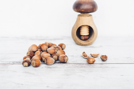 Hazelnuts in pile on wooden table with one mushroom-shaped nut in the nut-cracker and one nut cracked openの写真素材