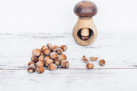 Hazelnuts in pile on wooden table with one mushroom-shaped nut in the nut-cracker and one nut cracked openの写真素材
