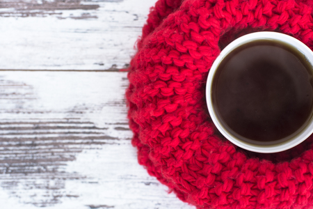 Cup of black tea on wooden table wrapped in bright-red warm scarf woven top viewの写真素材