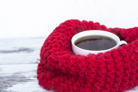 Cup of black tea on wooden table wrapped in bright-red warm woven scarfの写真素材