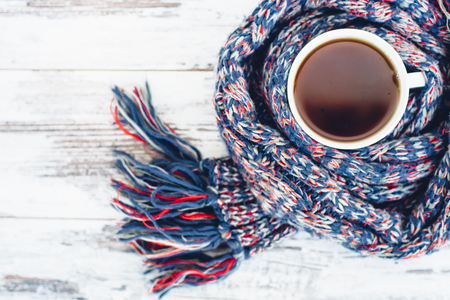 Cup of black tea on wooden table wrapped in warm scarf woven top viewの写真素材