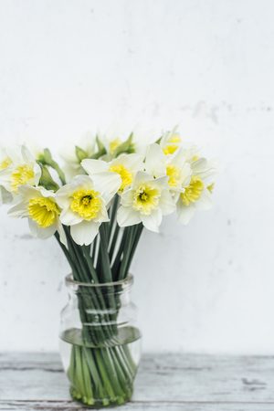 Bunch of narcissus in transparent vase on wooden tableの写真素材