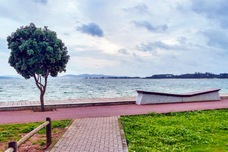 Bike and pedestrian lanes with bench on Vao boardwalk in Arousa island at stormの写真素材