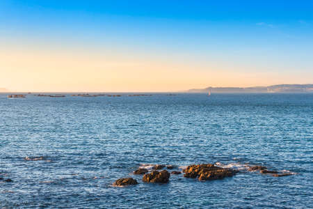 Rocks and mussel aquaculture rafts in Pontevedra estuary at dusk from Bueu coastの写真素材